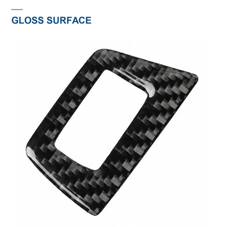 Angled close-up of a small window switch trim frame, showing its glossy carbon fiber surface and opening.